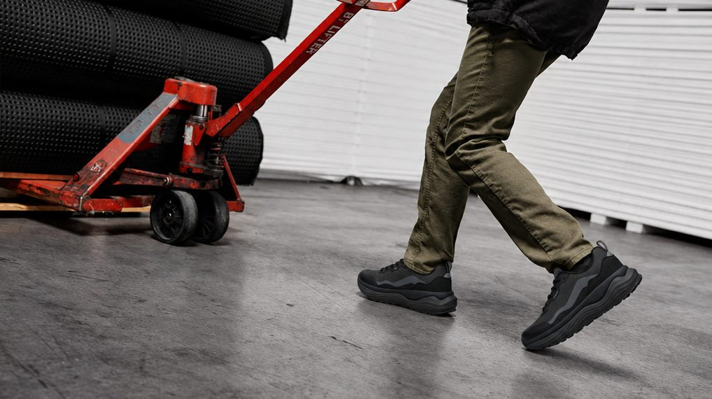 Worker in black sneakers pulling a pallet jack across a warehouse floor
