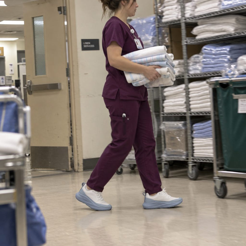 Nurse carrying folded linens down a hospital corridor