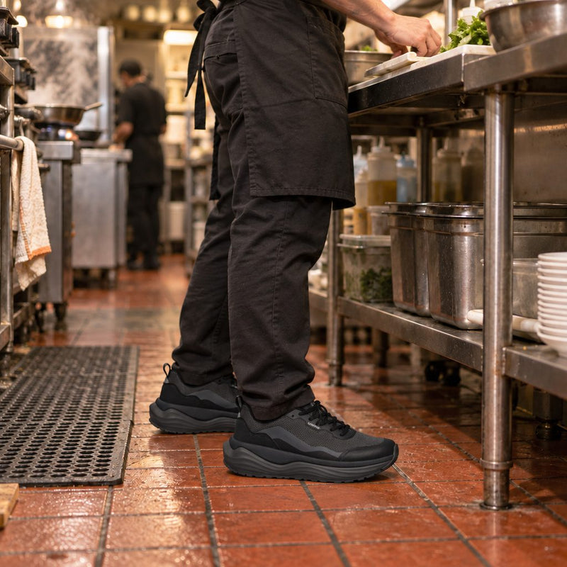 Cook in black sneakers standing at a station on a tiled kitchen floor