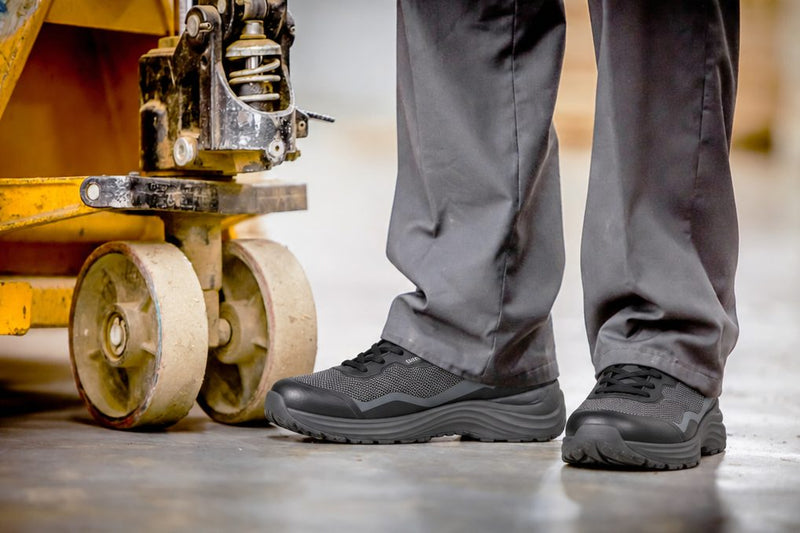 Black work sneakers beside a pallet jack on a warehouse floor