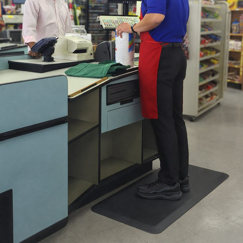 Cashier in black sneakers standing on a floor mat at a checkout counter